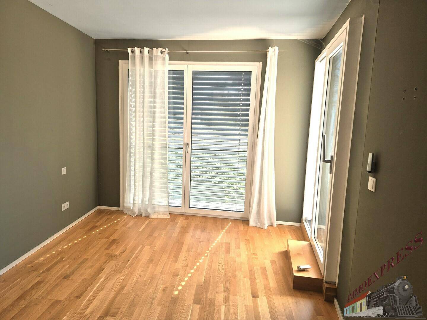 Heller Raum mit Holzparkettboden und großen Fenstern mit Jalousien, bereit zur individuellen Gestaltung.