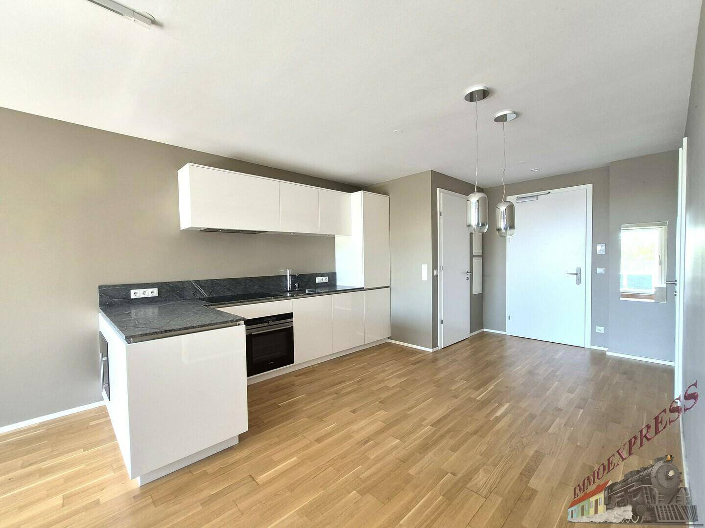 Moderne Einbauküche mit weißen Schränken, dunkler Arbeitsplatte und Holzparkettboden in offenem Design.