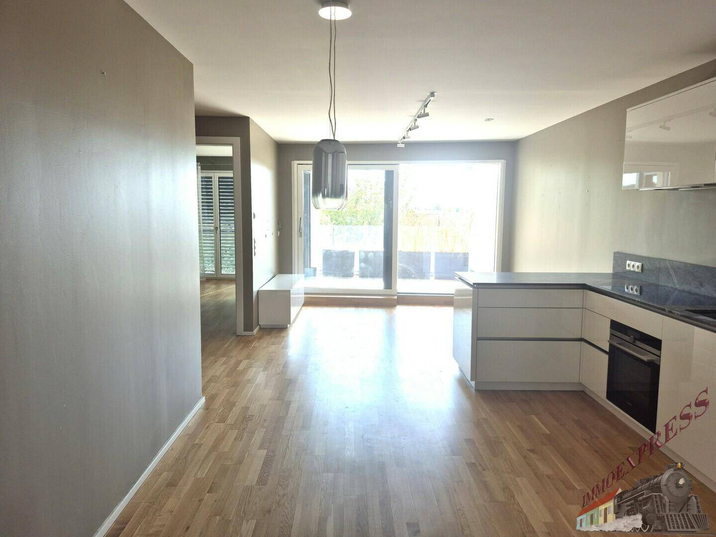 Offener Wohnbereich mit moderner Küche, Holzparkettboden und Zugang zum Balkon.