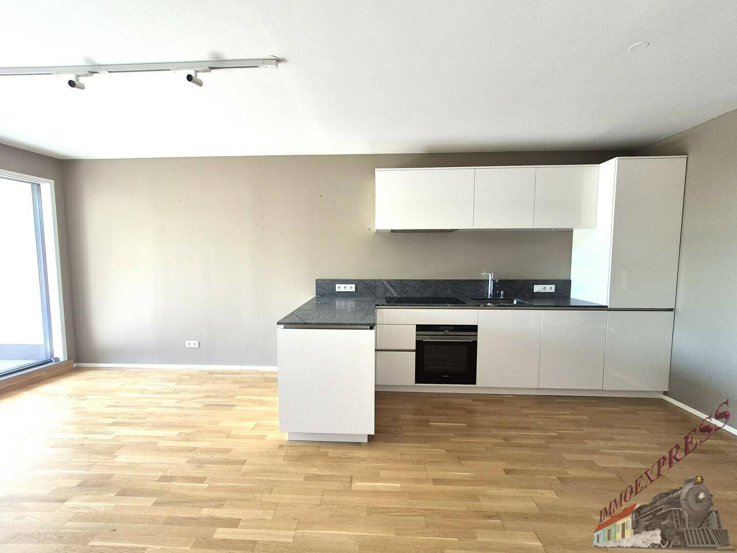 Helle, moderne Küche mit weißen Hochglanzfronten und dunkler Arbeitsplatte in offenem Wohnbereich.