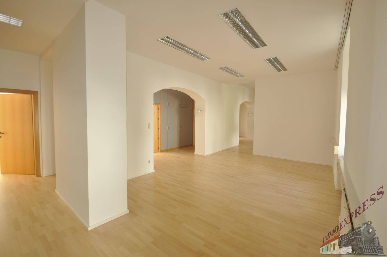 Geräumiger Bürobereich mit Holzboden, weißen Wänden und mehreren Türbögen.