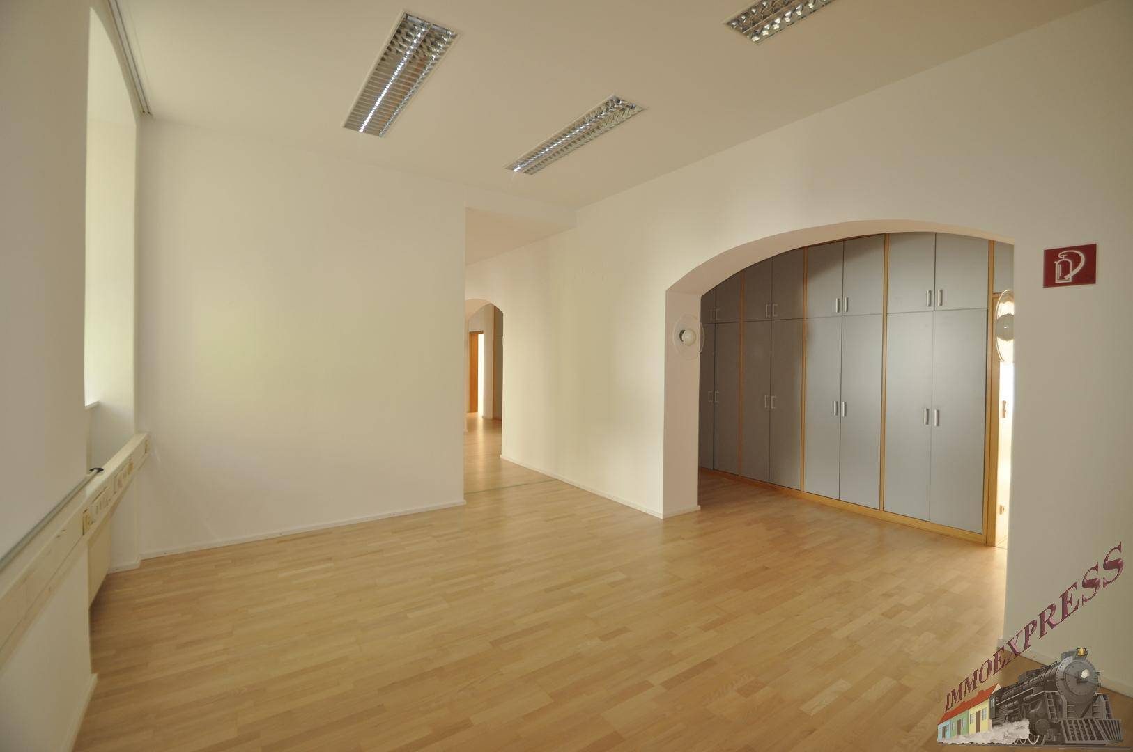 Heller Bürobereich mit Holzboden, weißen Wänden und einem großen Einbauschrank.