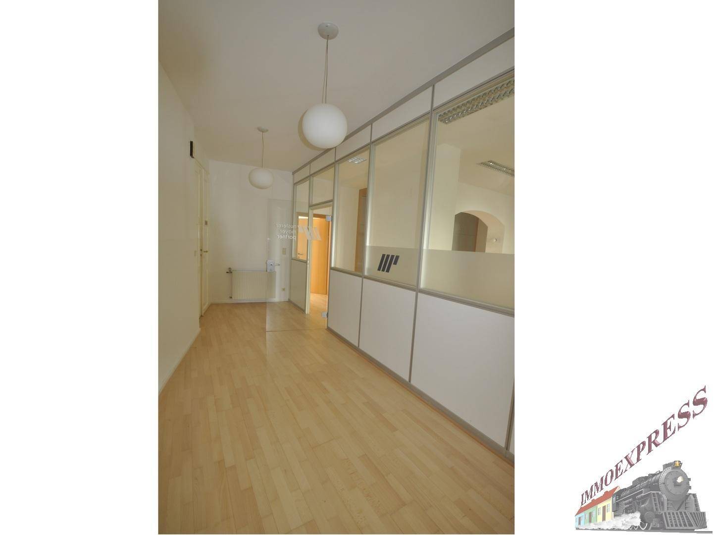 Flur oder Bürobereich mit Holzboden und Glasabtrennungen, die zu weiteren Räumen führen.