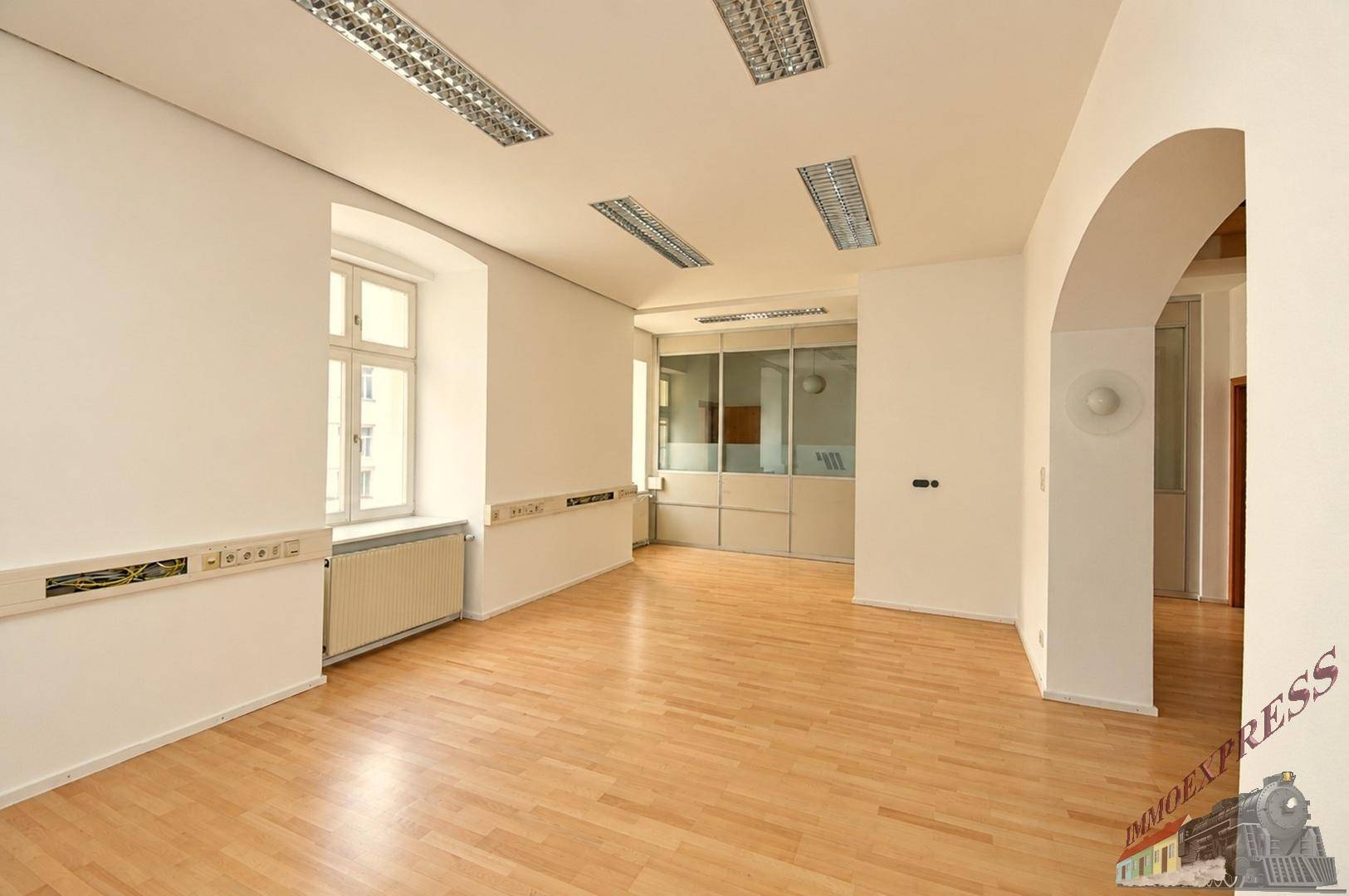 Großraumbüro mit Holzboden, weißen Wänden und Glasabtrennungen zu weiteren Büros.