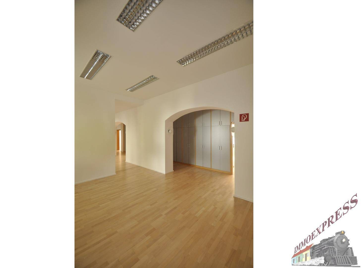 Heller Bürobereich mit Holzboden, weißen Wänden und einem großen Einbauschrank.