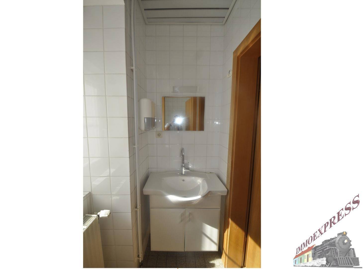 Toilettenraum mit weißen Fliesen, Waschbecken und Spiegel, in gutem Zustand.