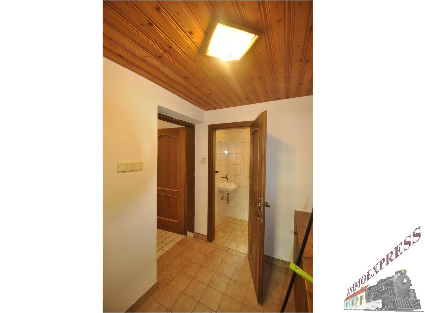 Flur mit Fliesenboden und Holzpaneeldecke, der zu einem kleinen Badezimmer führt.