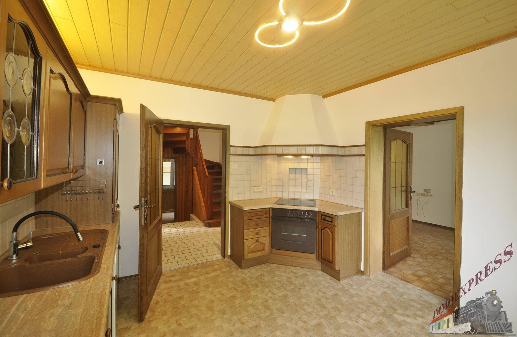 Traditionelle Küche mit Holzschränken, Fliesenboden und einer Holzpaneeldecke, mit Blick auf die Treppe.