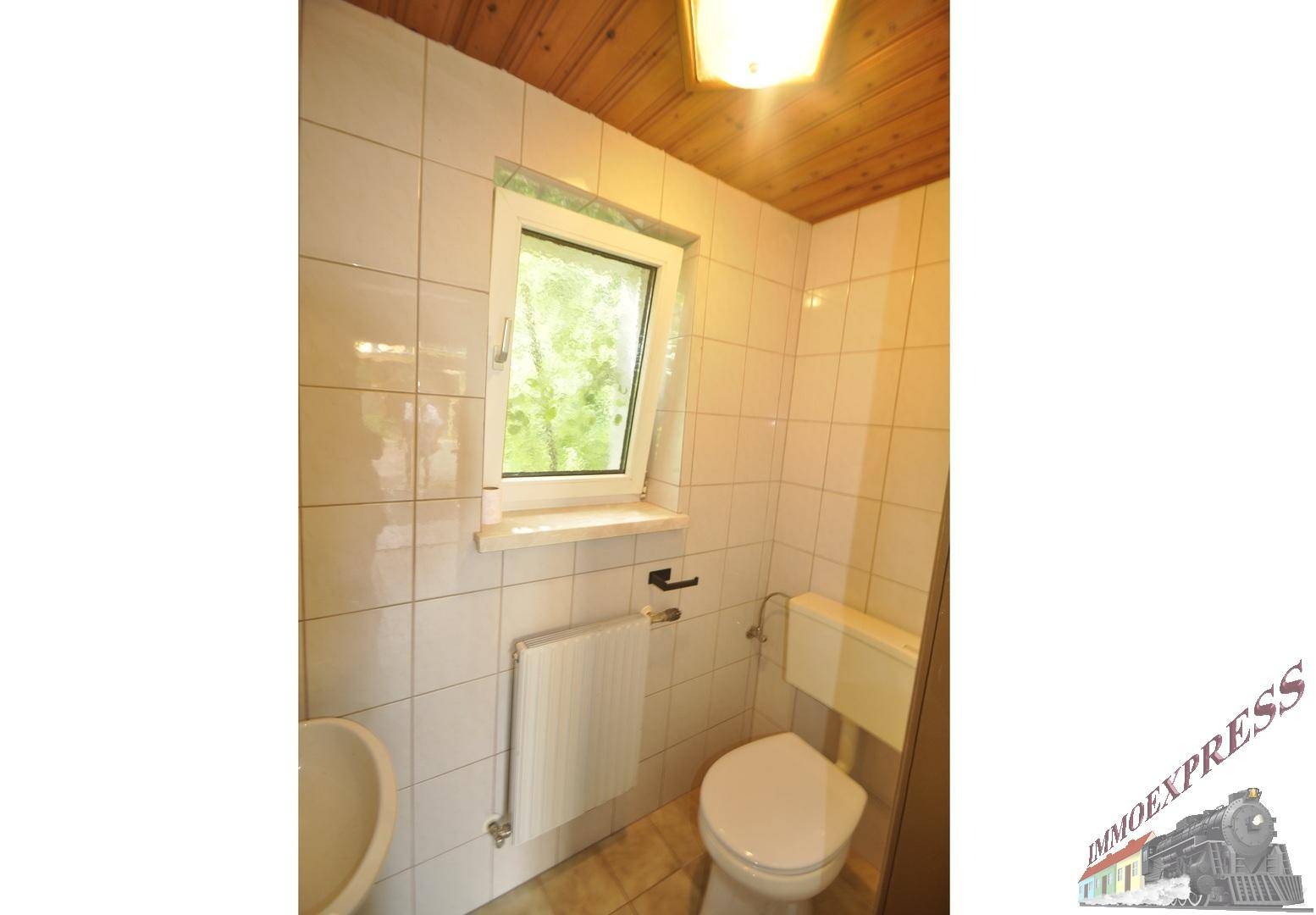 Kleines WC mit weißen Fliesen, Toilette, Waschbecken und einem Fenster für Tageslicht.