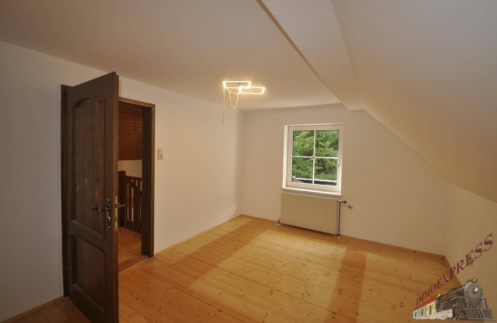 Geräumiges Schlafzimmer mit Holzdielenboden und schräger Decke, Zugang zum Flur.