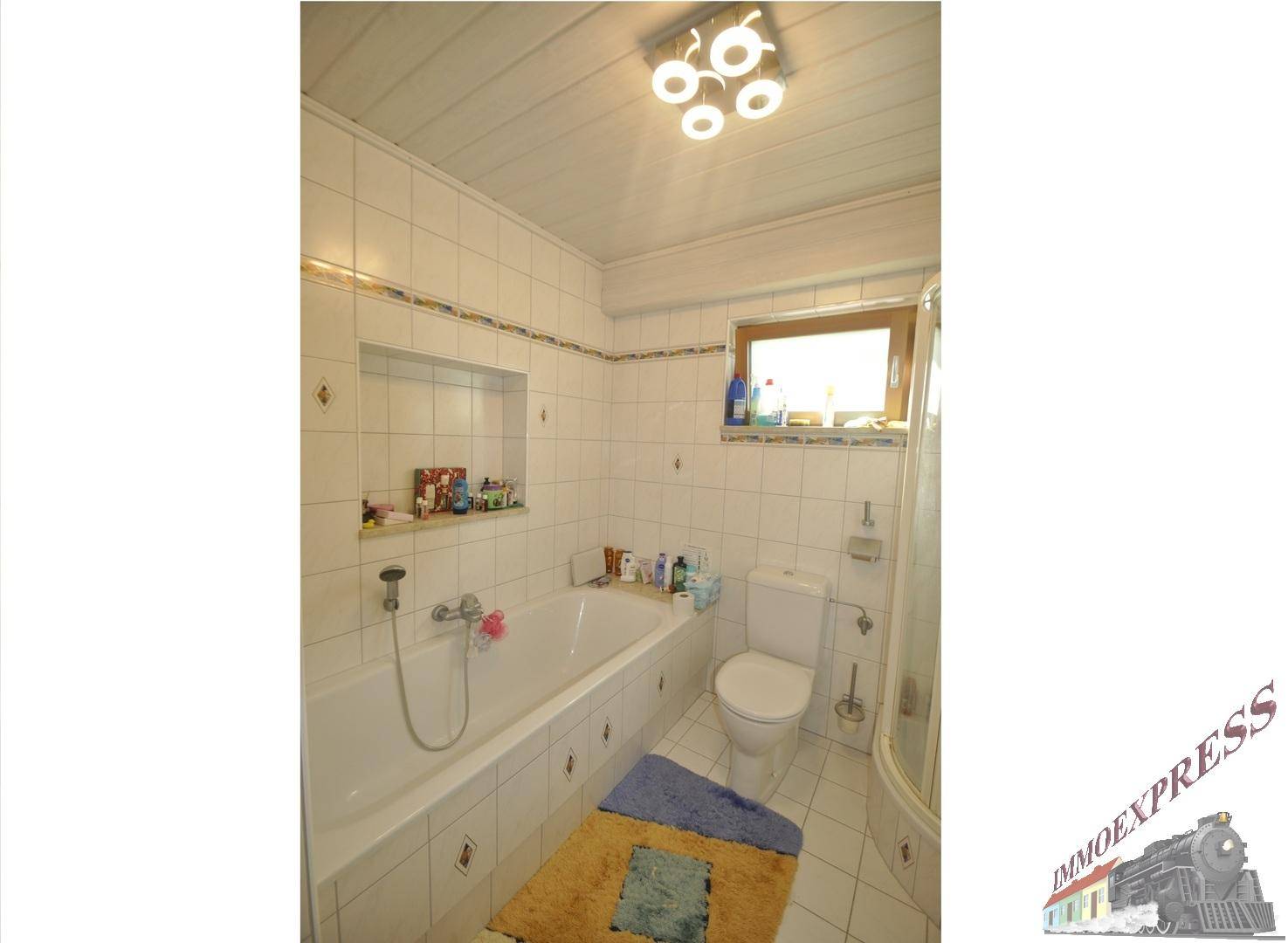 Helles Badezimmer mit Badewanne, Toilette und Fenster, komplett gefliest.