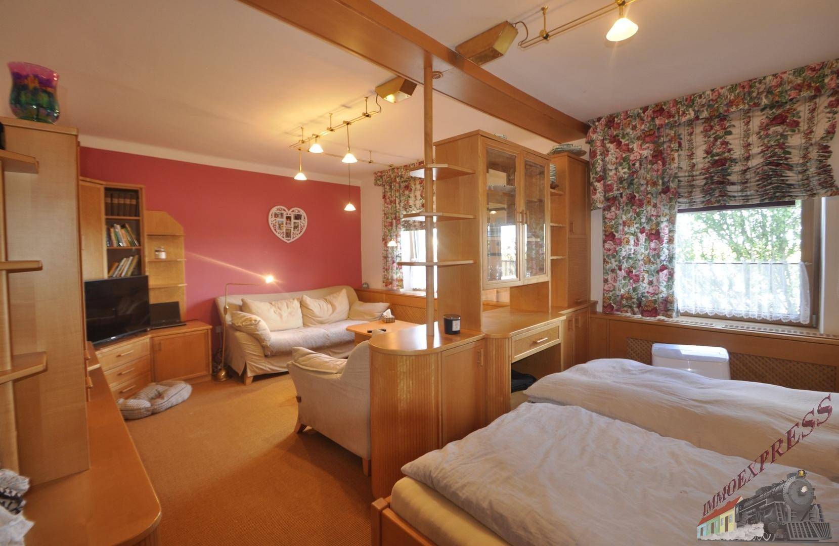 Schlafzimmer mit Doppelbett, Sofa und Holzmöbeln, durch eine Trennwand unterteilt.