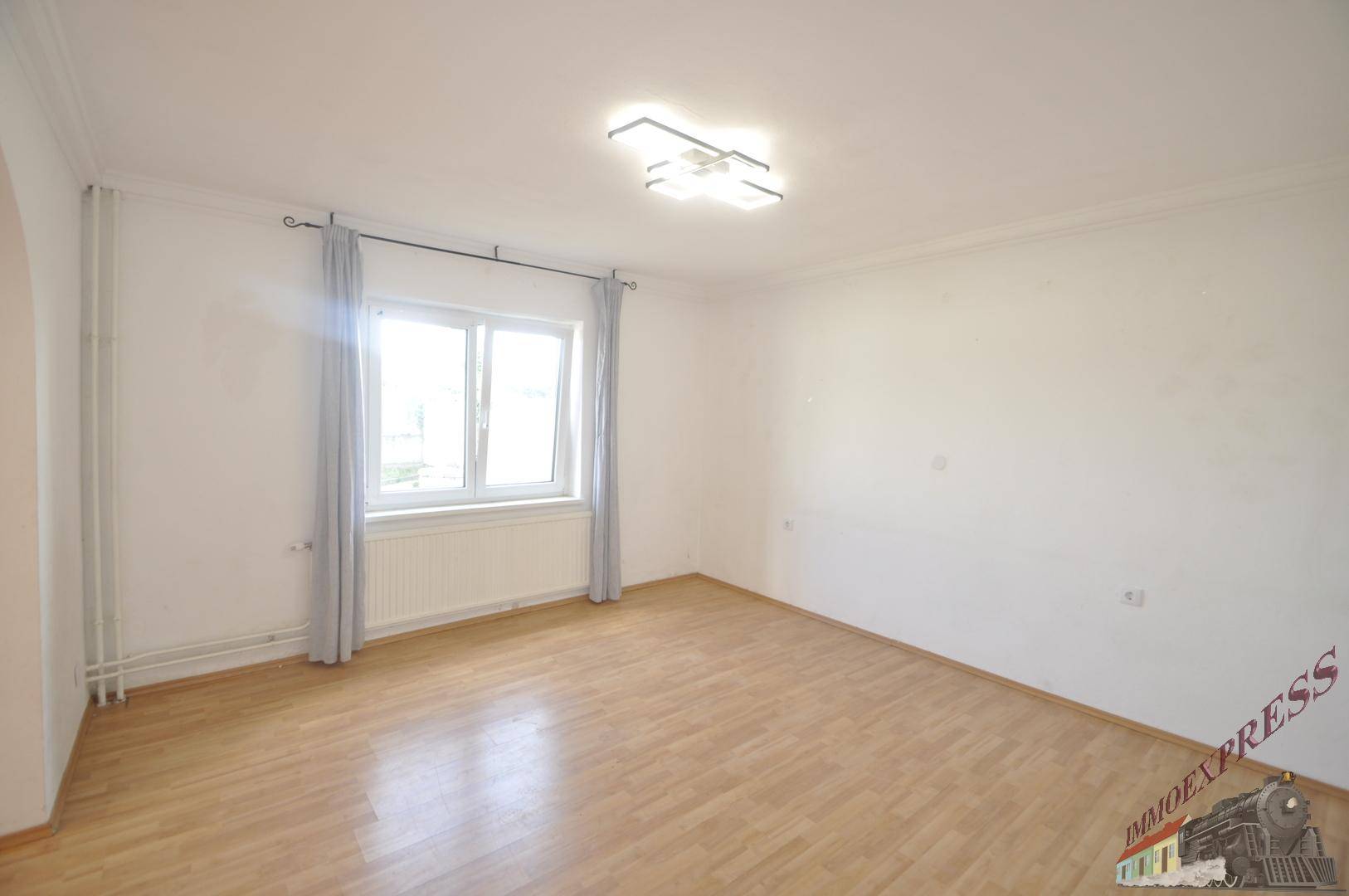 Freundliches Wohnzimmer mit Laminatboden, weißen Wänden und einem großen Fenster für viel Tageslicht.