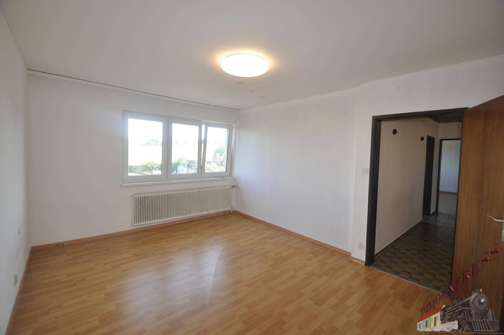 Geräumiges Schlafzimmer mit Laminatboden, weißen Wänden und Zugang zum Flur.