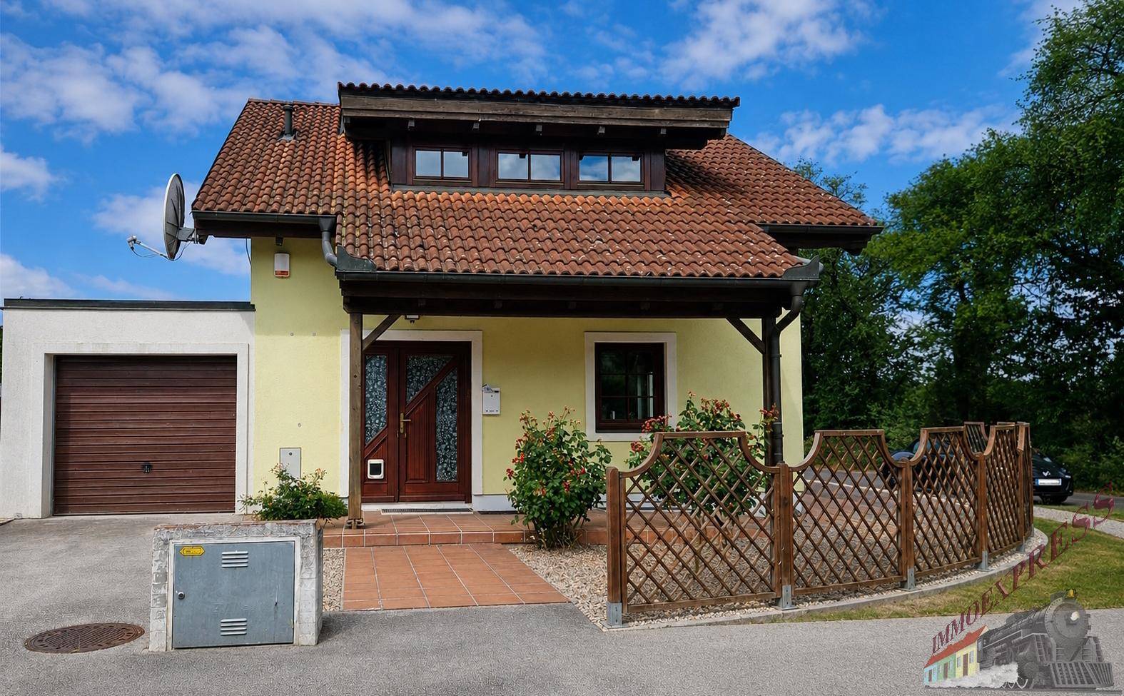 Gelbes Einfamilienhaus mit rotem Ziegeldach, Garage und gepflegtem Vorgarten.