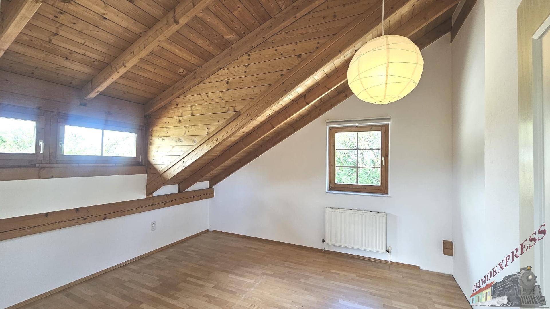 Helles Schlafzimmer im Dachgeschoss mit Holzbalkendecke und Ausblick.
