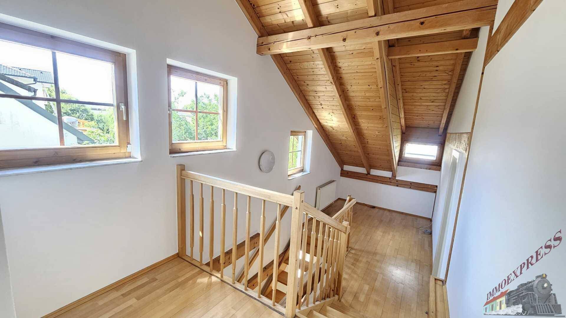 Treppenaufgang zum Dachgeschoss mit Holzgeländer und schrägen Decken.