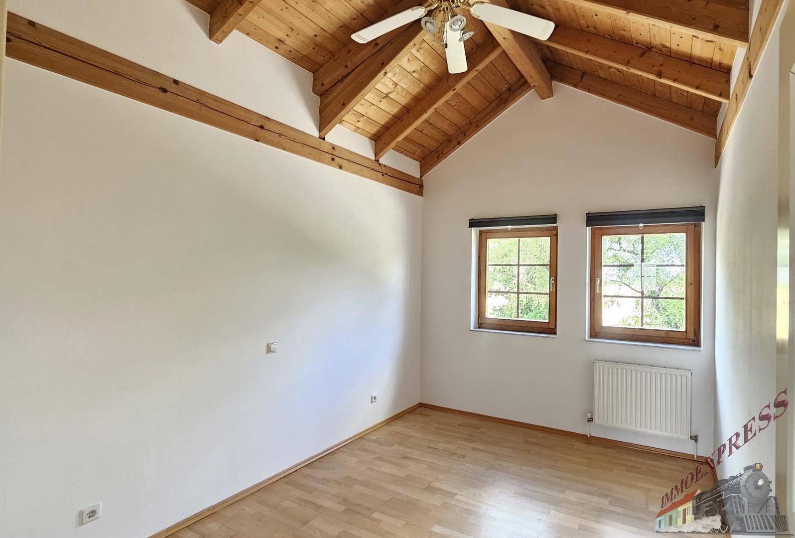 Geräumiges Schlafzimmer mit hohen Decken, Holzbalken und Deckenventilator.