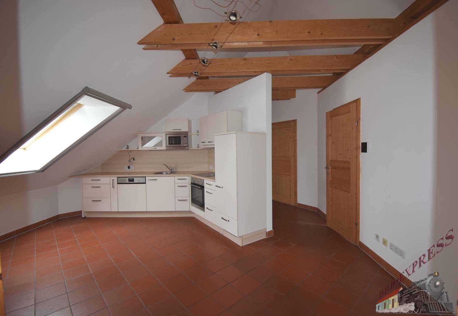 Offene Küche im Dachgeschoss mit weißen Schränken, Fliesenboden und sichtbaren Holzbalken.