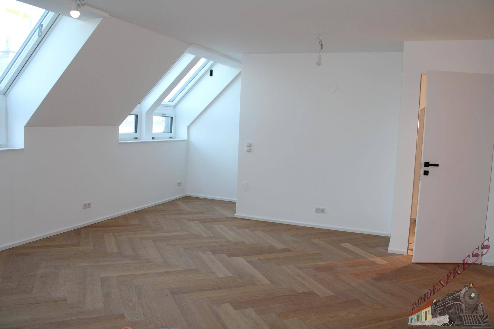 Geräumiges Dachgeschosszimmer mit schrägen Wänden, hellem Fischgrätparkett und Dachfenstern.