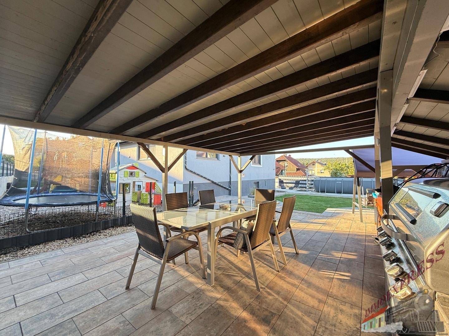 Überdachte Terrasse mit Esstisch, Stühlen und Grillbereich im Garten.