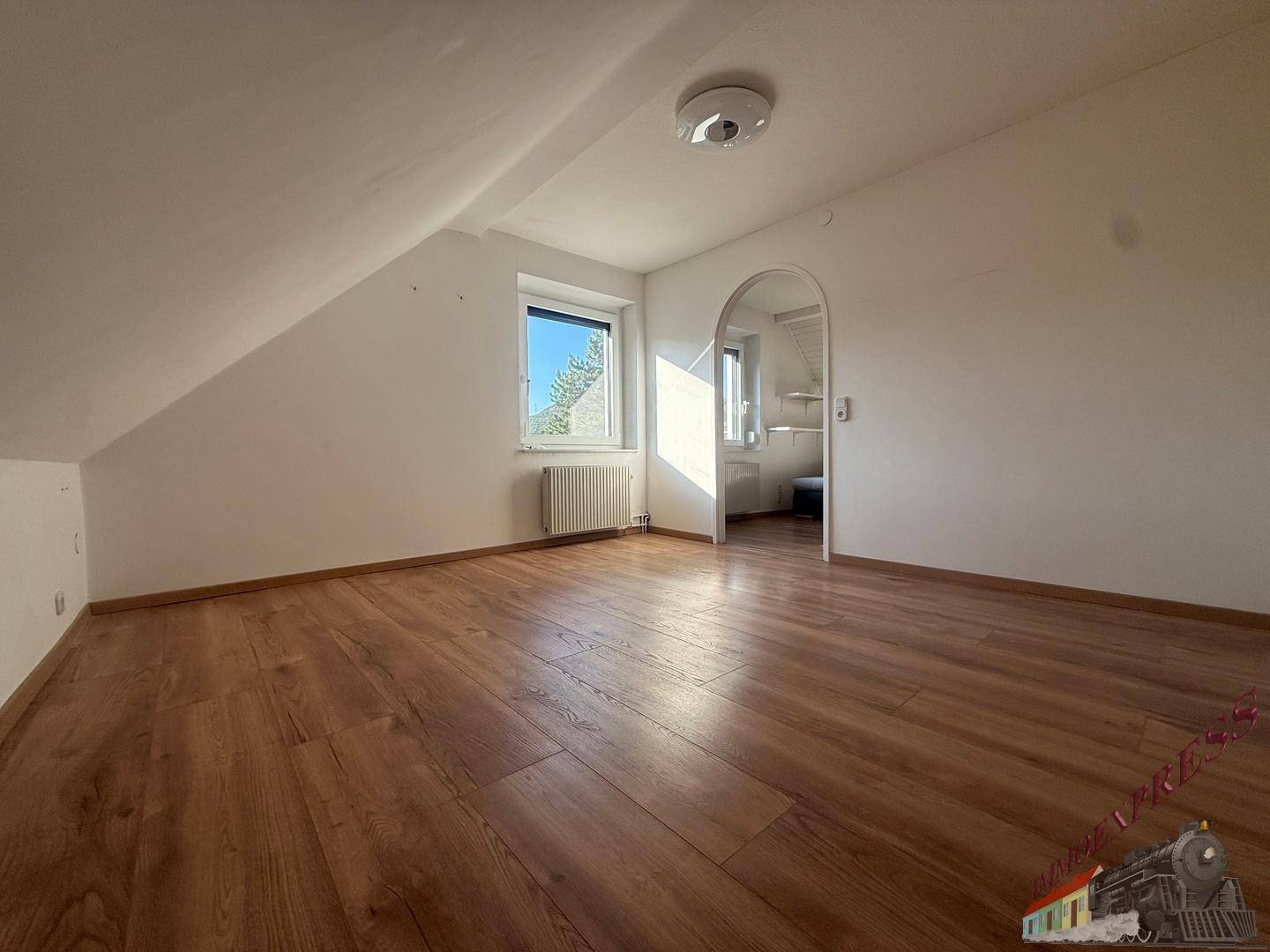Leerer Raum im Dachgeschoss mit Holzboden und schrägen Wänden.