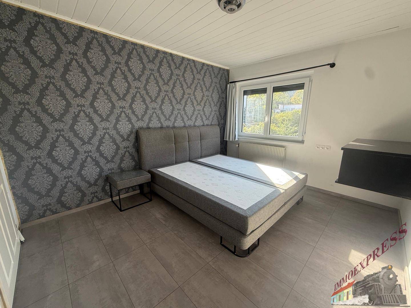 Schlafzimmer mit Doppelbett, gemusterter Tapete und Fliesenboden.