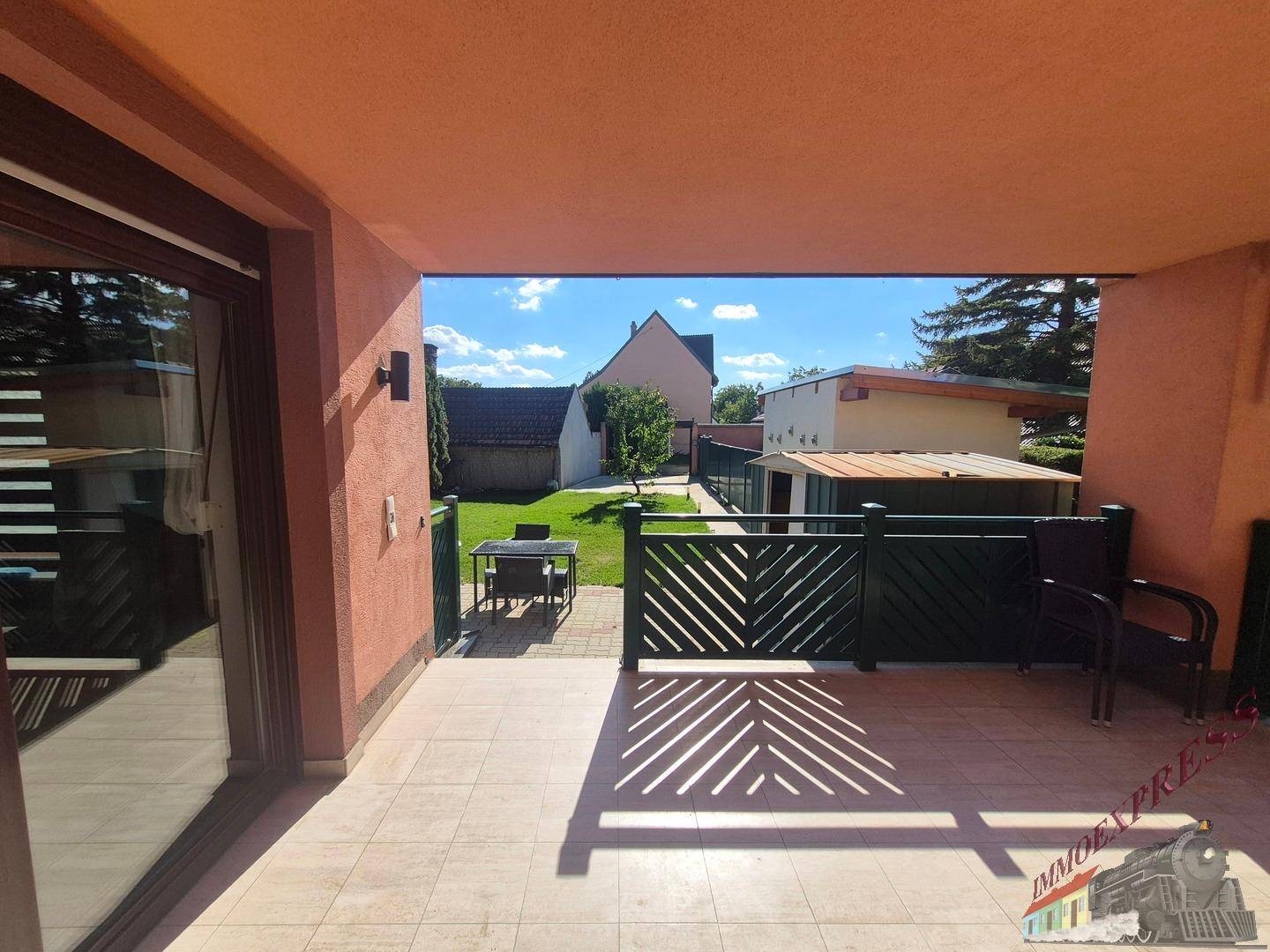 Überdachte Terrasse mit Fliesenboden und Blick auf den sonnigen Gartenbereich.