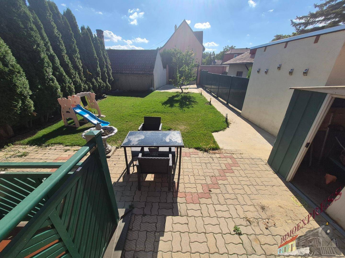 Sonniger Terrassenbereich mit Sitzgelegenheiten, Rasenfläche und Gartenhaus.