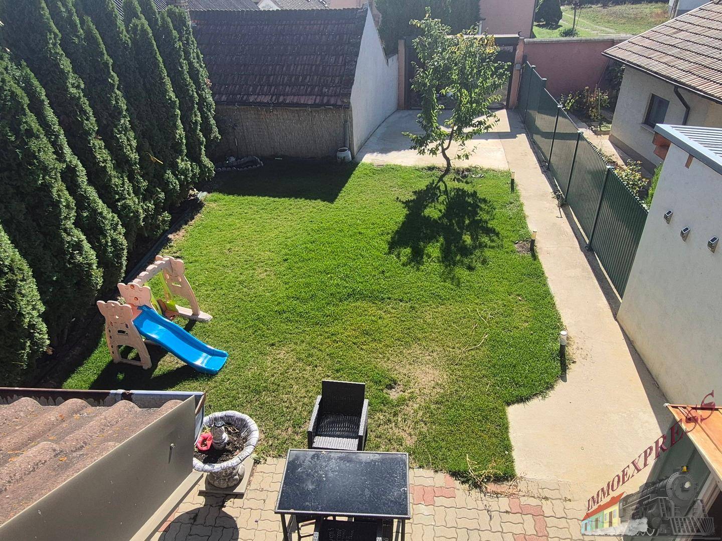 Gepflegter Garten mit Rasenfläche, Spielgeräten und einem kleinen Baum.