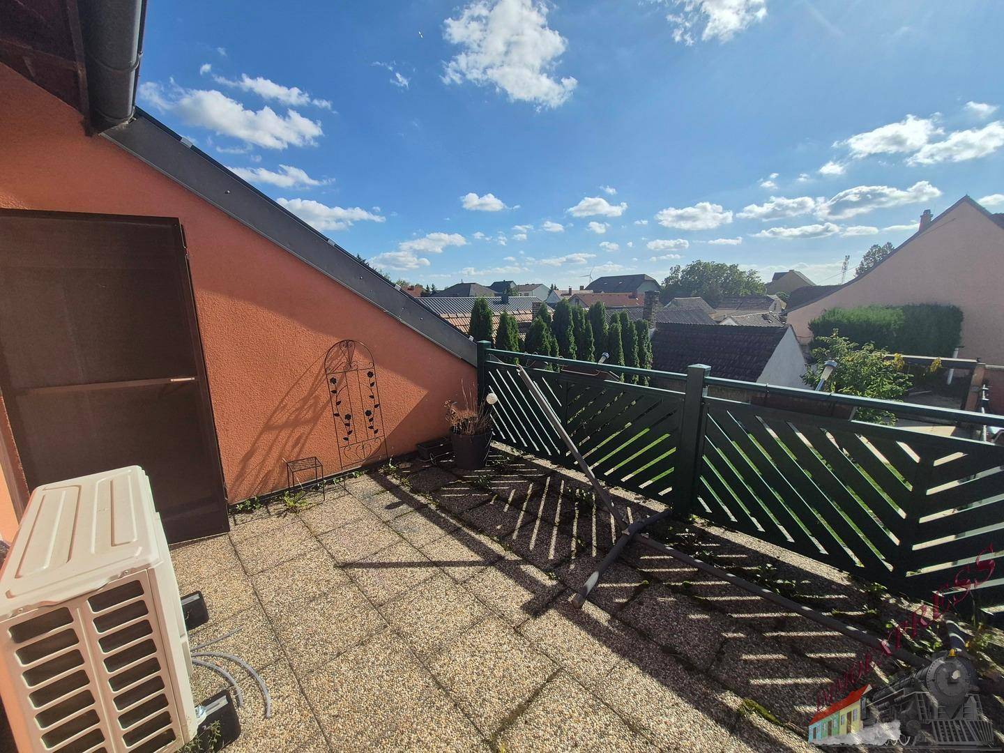 Sonniger Balkon mit Fliesenboden, grüner Brüstung und Blick über die Nachbarschaft.