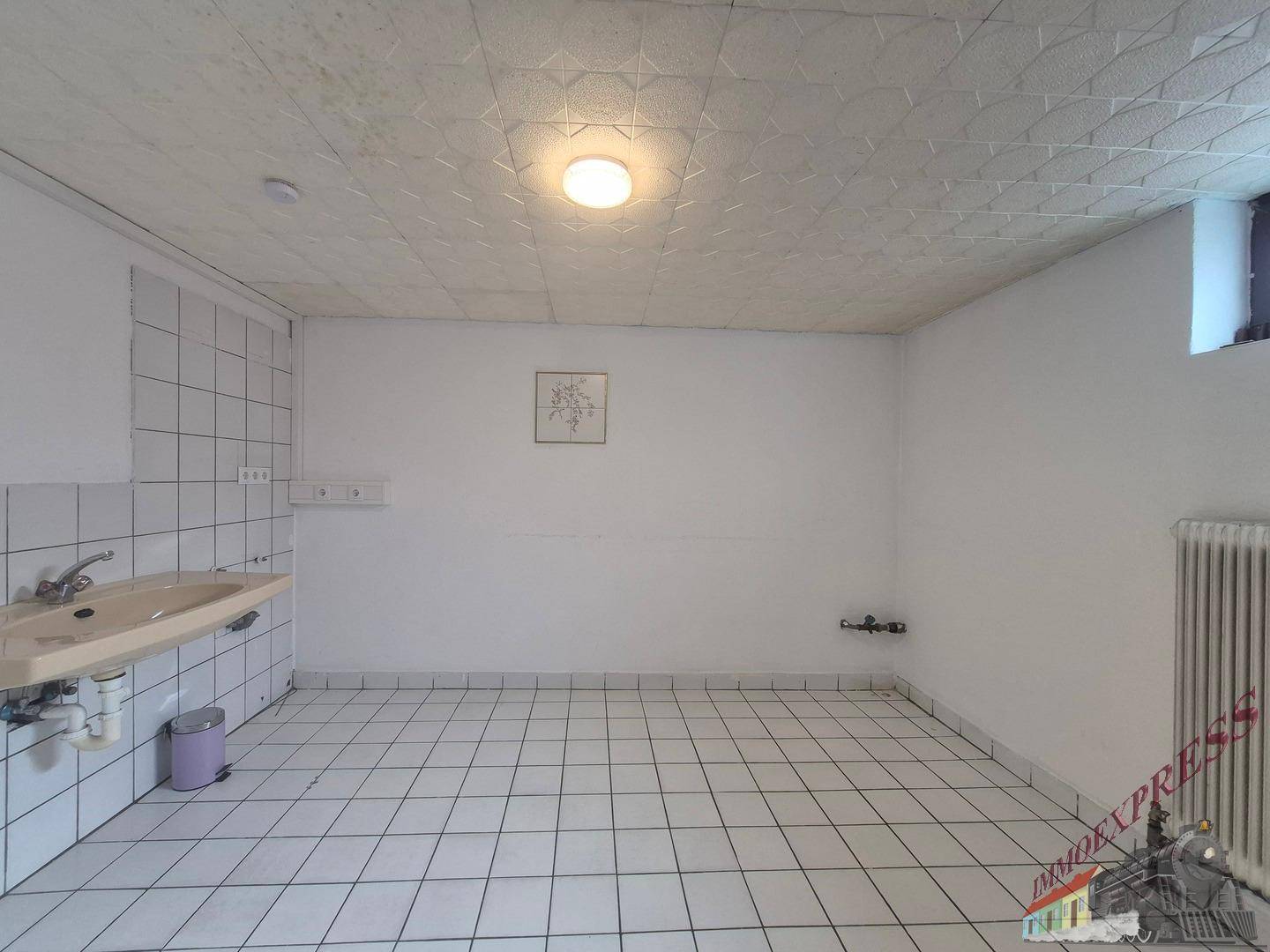 Kellerraum mit Fliesenboden, Waschbecken und Heizkörper, ideal als Hauswirtschaftsraum.
