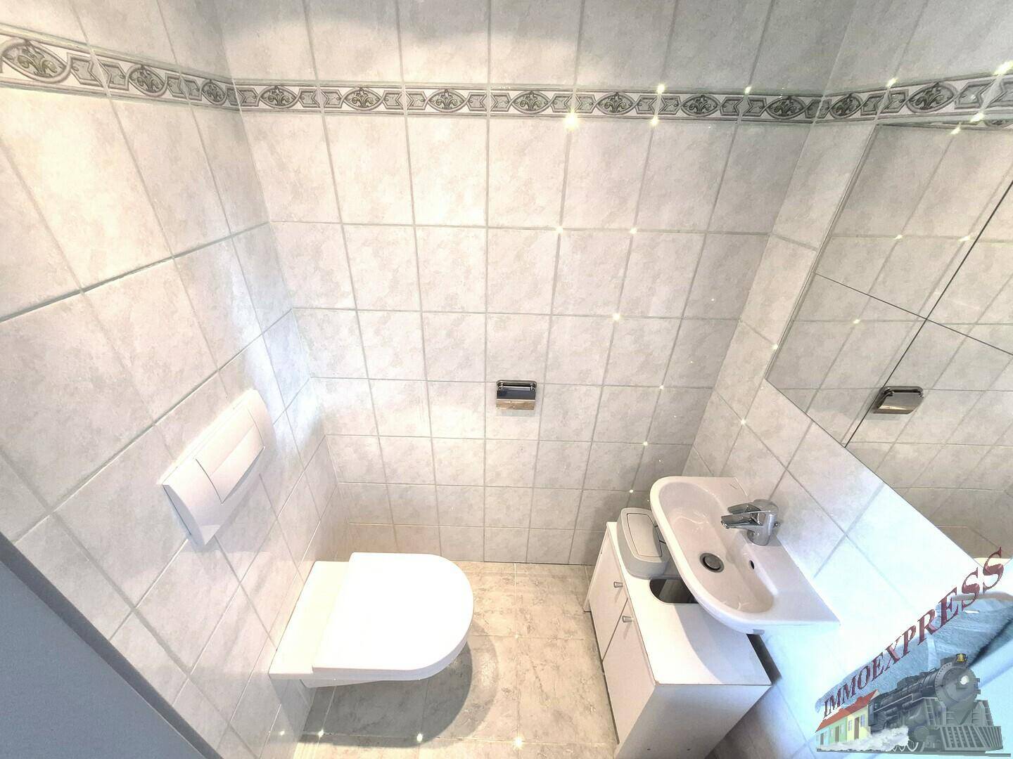Kleines Gäste-WC mit Wand-WC, Waschbecken und hellen Fliesen an Wänden und Boden.