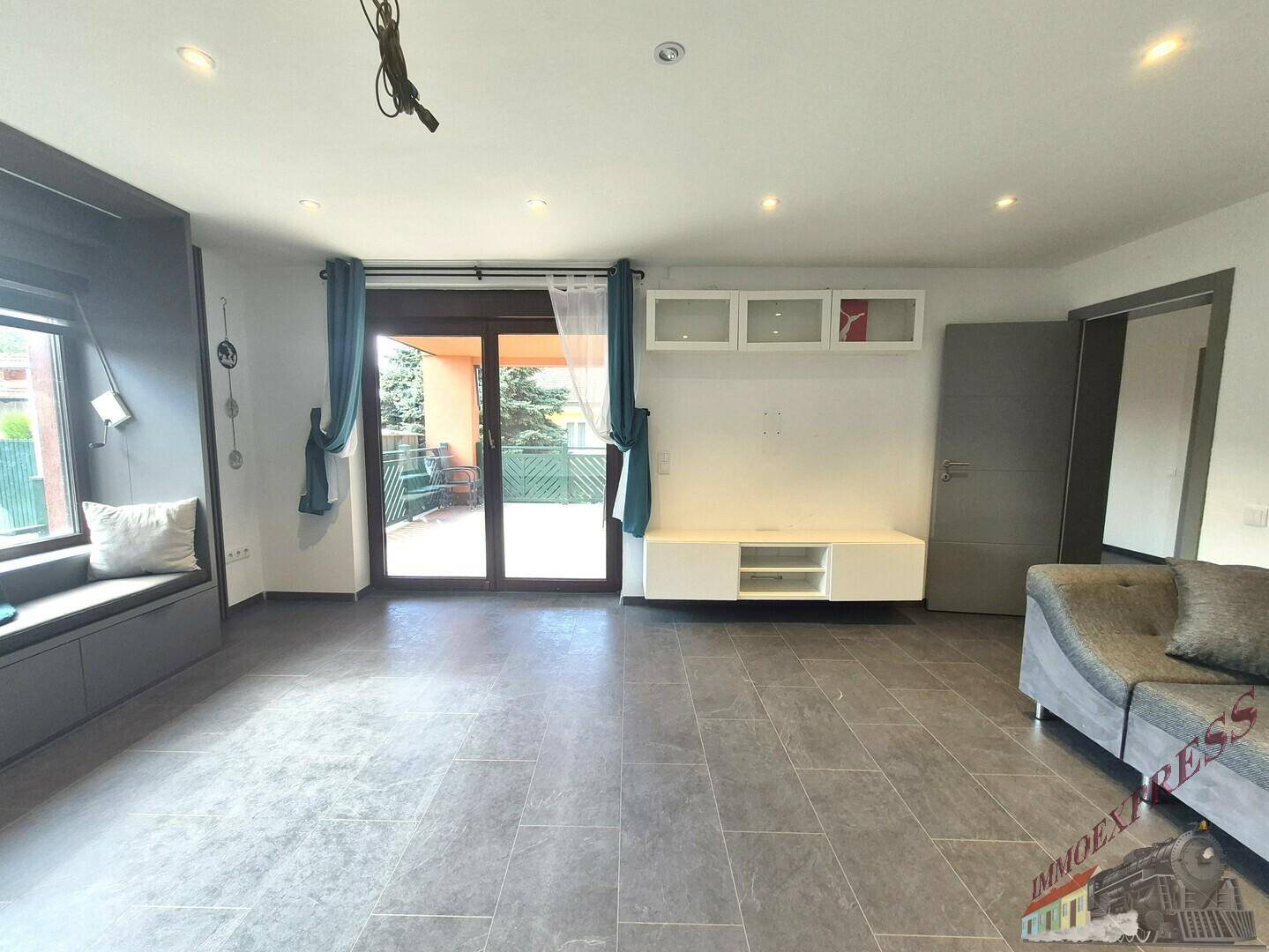 Helles Wohnzimmer mit Fliesenboden, Zugang zur Terrasse und einem Sofa.