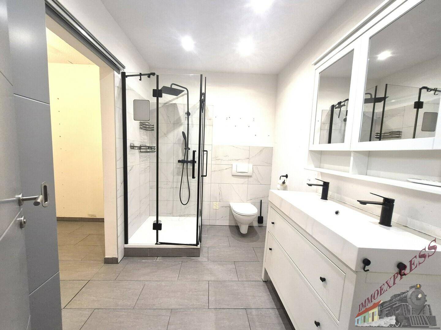 Modernes Badezimmer mit großer Duschkabine, Doppelwaschbecken und hellen Fliesen.