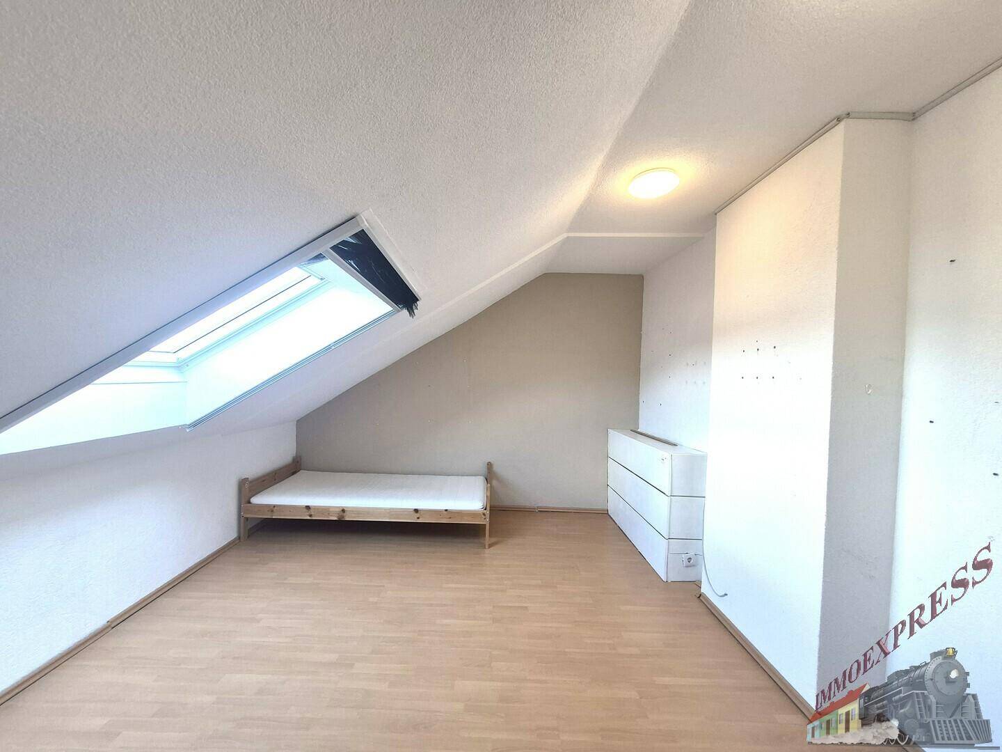 Gemütliches Dachgeschosszimmer mit Holzbett, Holzfußboden und einem Dachfenster.