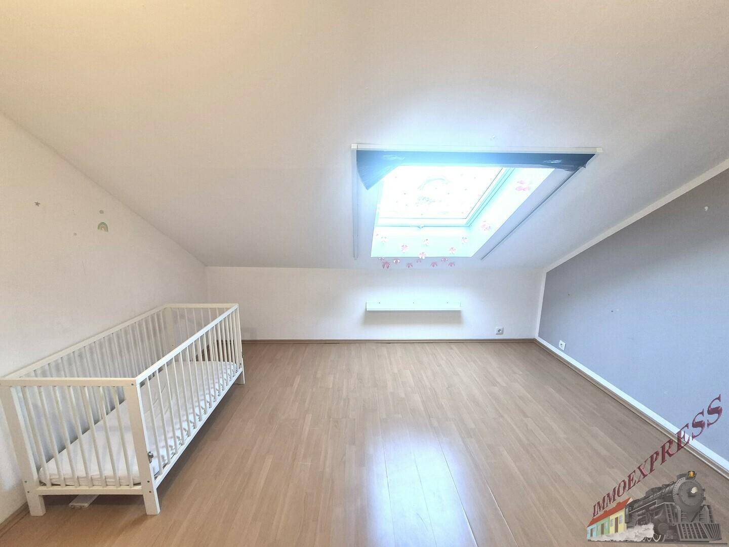 Dachgeschosszimmer mit Babybett, Holzfußboden und großem Dachfenster für viel Tageslicht.