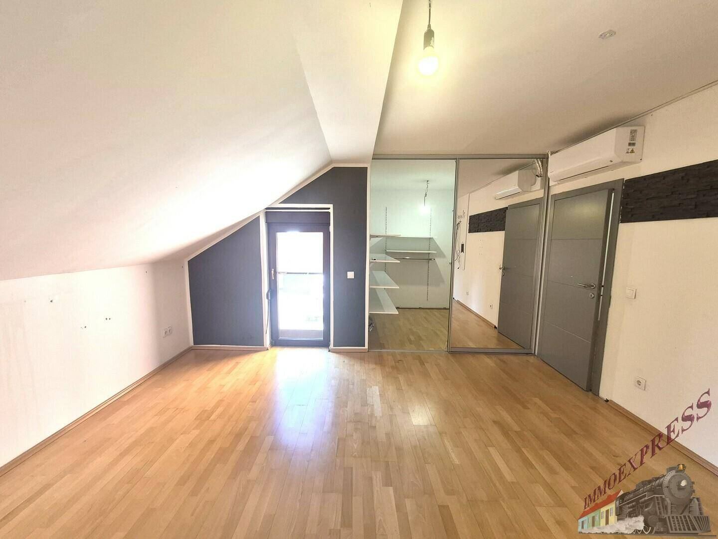 Helles Dachgeschosszimmer mit Holzfußboden, Dachschräge und integriertem Spiegelschrank.