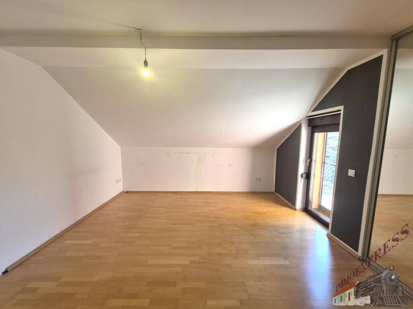 Geräumiges Dachgeschosszimmer mit Holzfußboden, Dachschräge und Zugang zum Balkon.