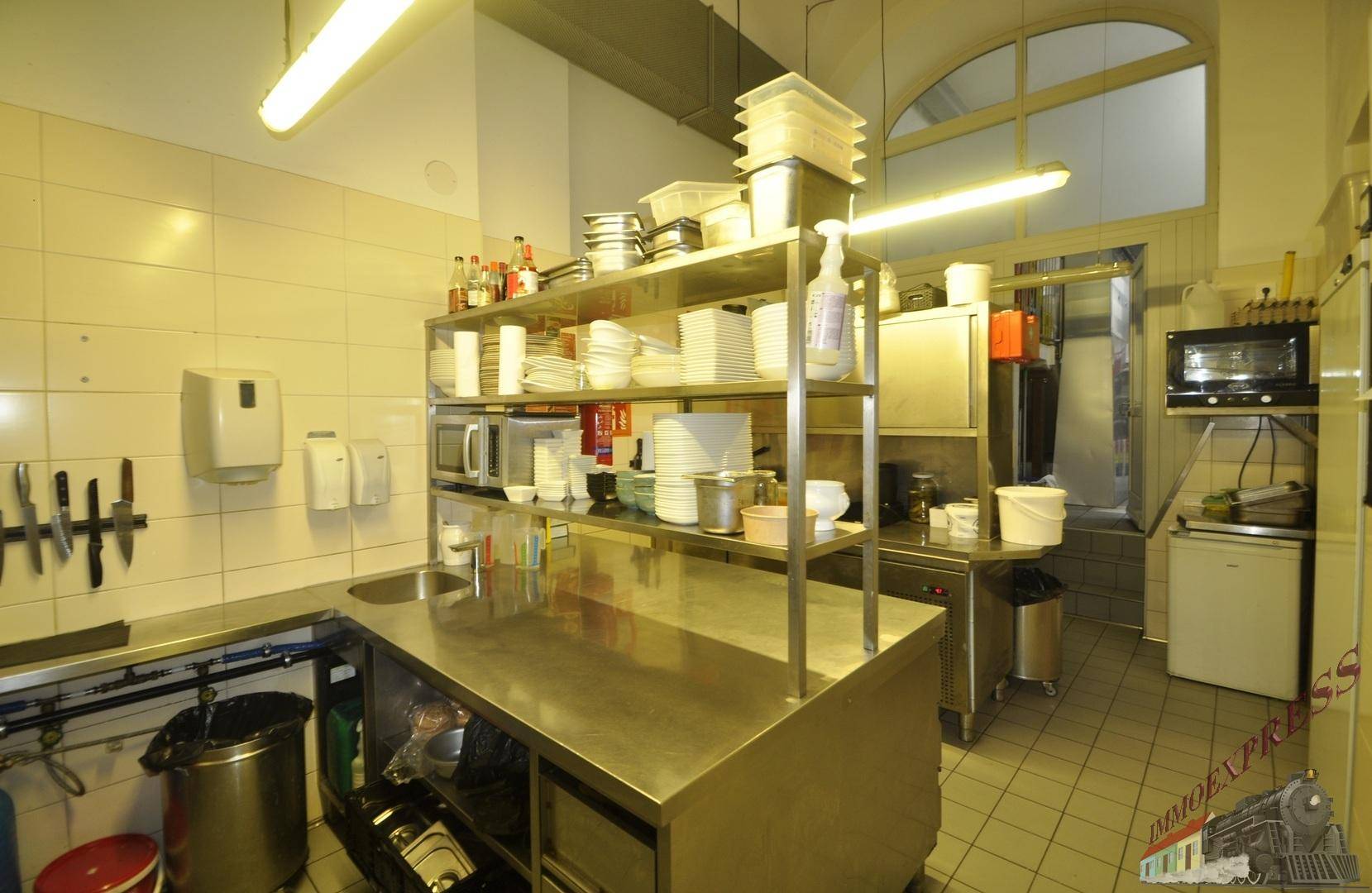 Professionelle Großküche mit Edelstahloberflächen, Regalen und industriellen Geräten.