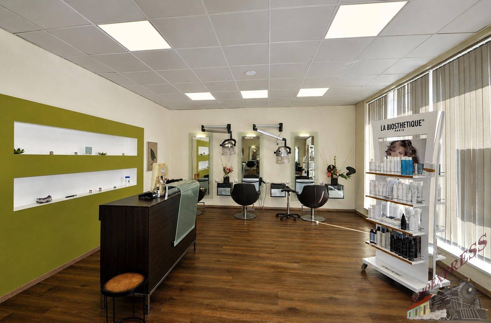 Empfangsbereich eines Friseursalons mit Produktregalen, Holzboden und hellgrüner Akzentwand, gut beleuchtet.