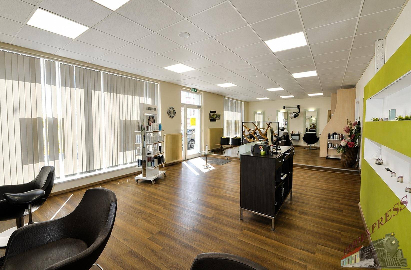 Geräumiger Friseursalon mit großen Fenstern, Holzfußboden und moderner Einrichtung, hell und einladend.