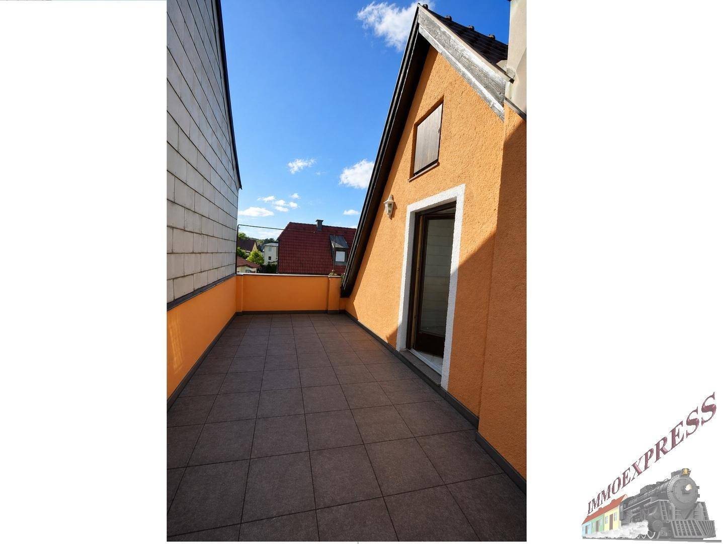 Sonniger Terrassenbereich mit orangefarbener Fassade und Fliesenboden, ideal zum Entspannen.