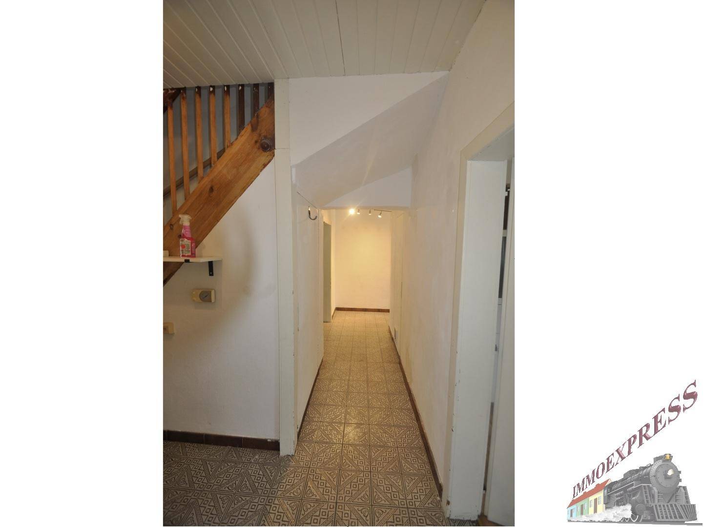 Langer Flur mit gemusterten Fliesen, Holztreppe und Zugang zu weiteren Räumen im Haus.