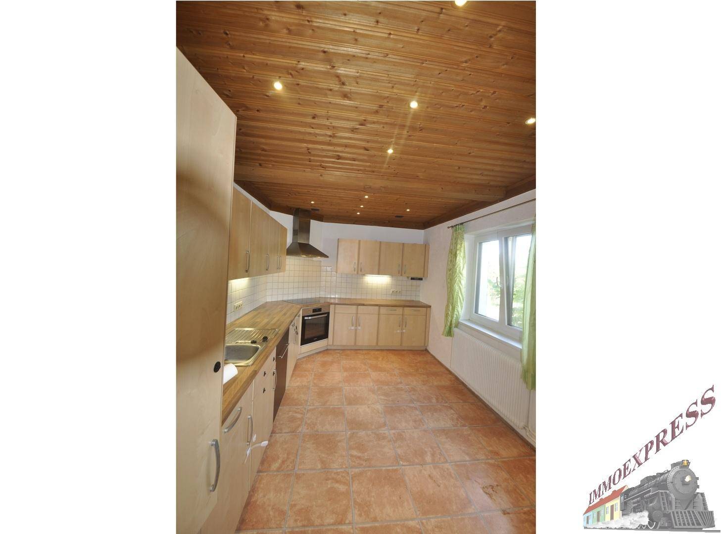 Geräumige Küche mit Holzdecke, funktionaler Einbauküche und Blick nach draußen durch das Fenster.