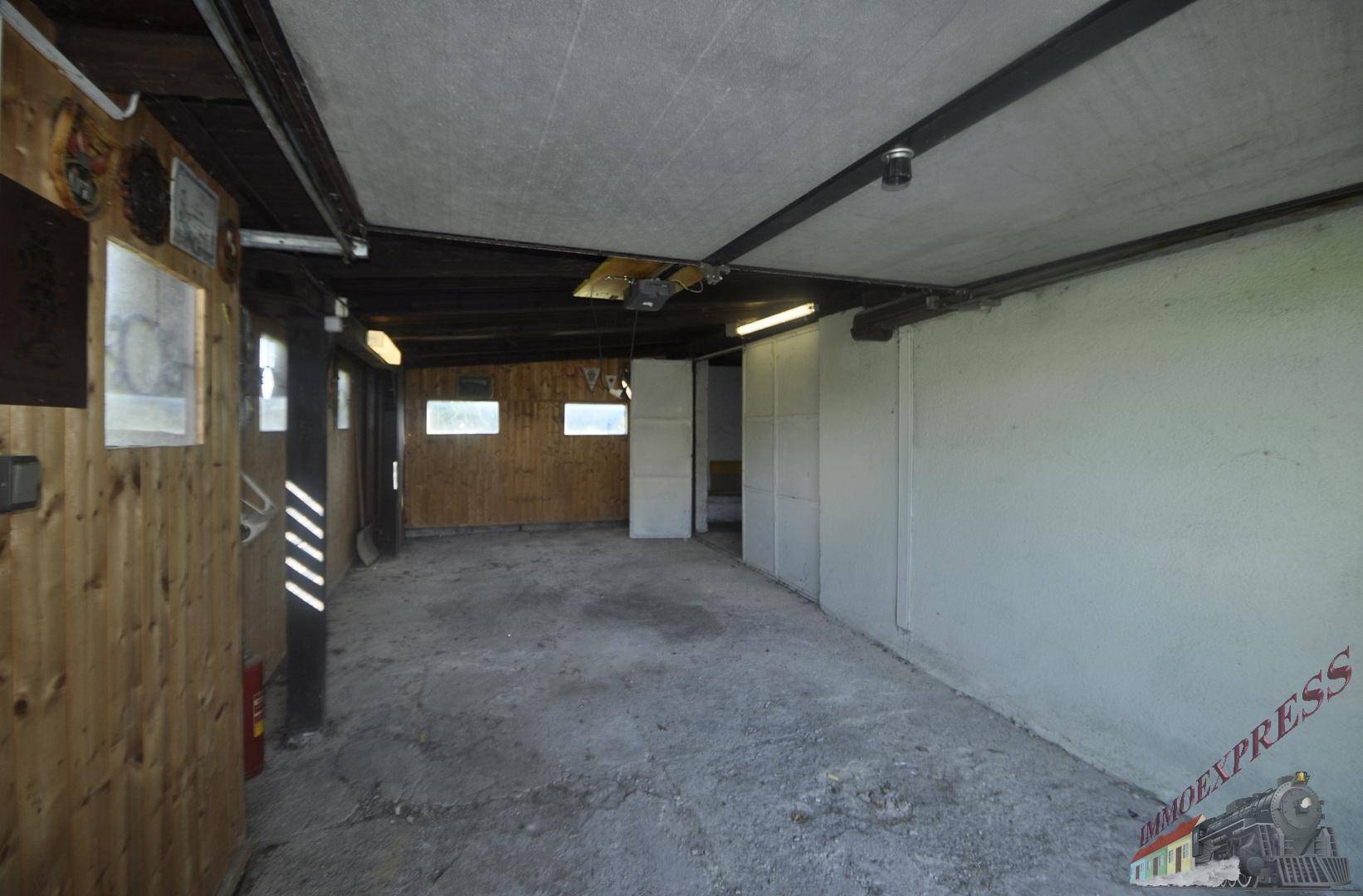 Geräumige Garage oder Werkstatt mit Betonboden und Holzverkleidung, bereit zur Nutzung.
