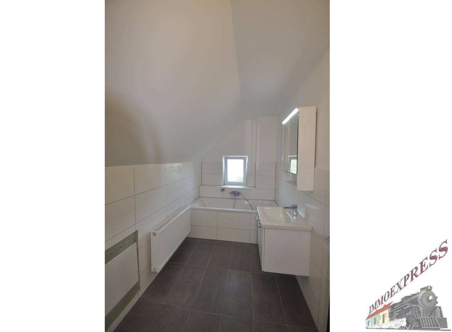 Modernes Badezimmer mit Badewanne, Waschbecken und Spiegelschrank unter schräger Decke.