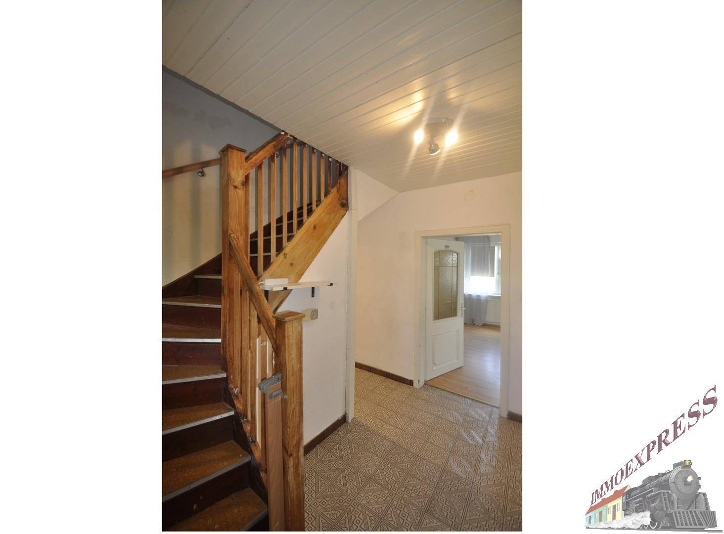 Eingangsbereich mit Holztreppe, gemusterten Fliesen und Zugang zu einem hellen Zimmer.