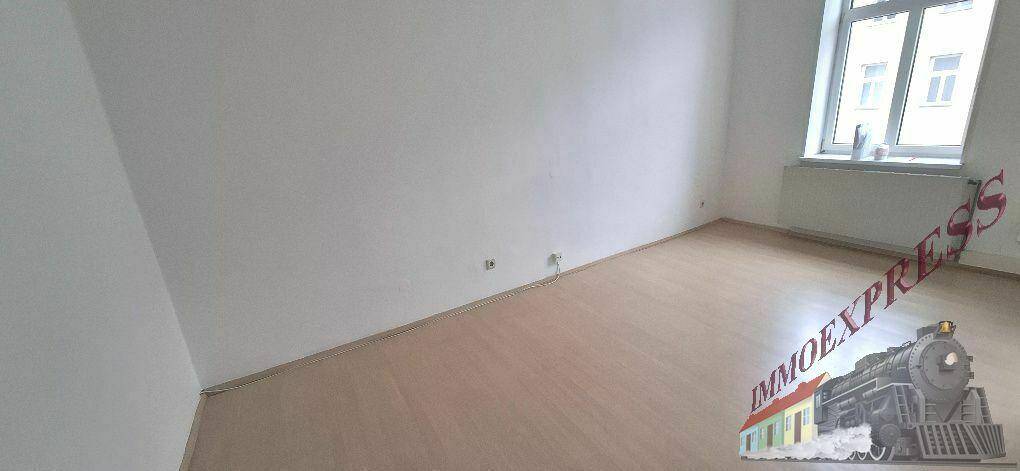 Heller Raum mit schlichten weißen Wänden und hellem Laminatboden, gut beleuchtet durch ein Fenster.