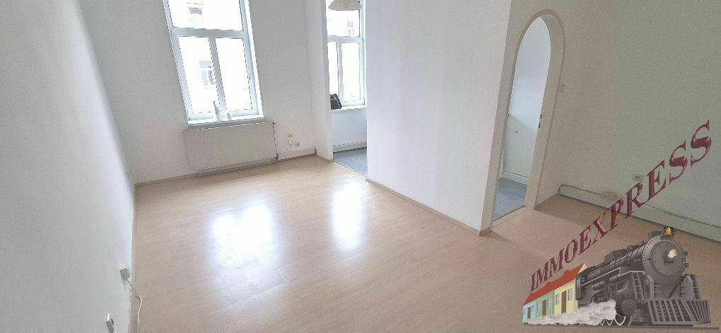 Geräumiges Zimmer mit hellen Laminatböden und Heizkörper unter den großen Fenstern.